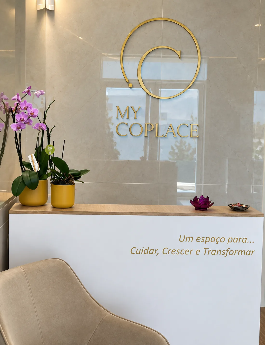 Hall de entrada do edifício, com balcão de recepção, orquídeas e o letreiro do espaço.